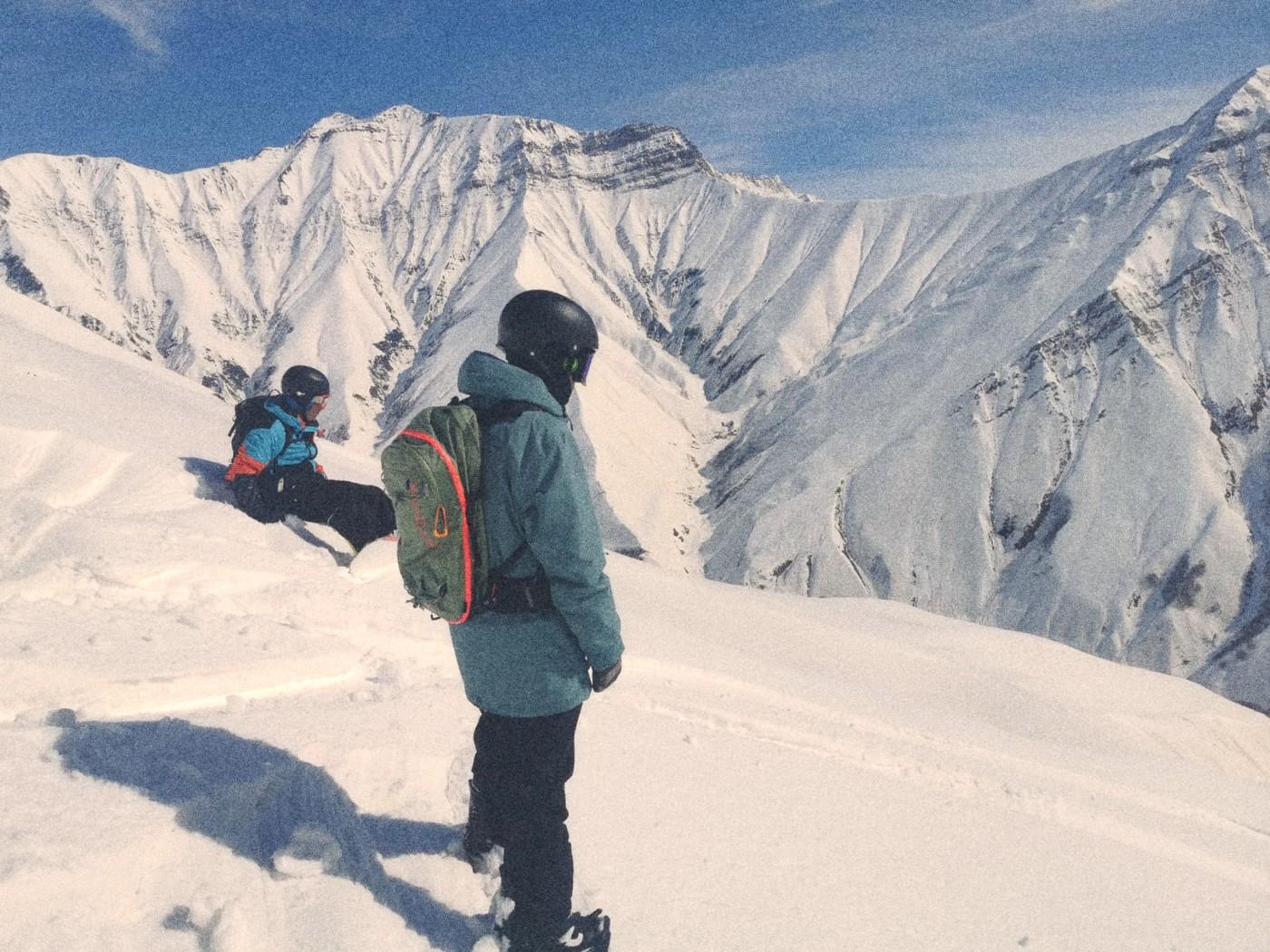 Two freeriders on a ridge in the Gudauri backcountry, looking over the terrain before dropping in.