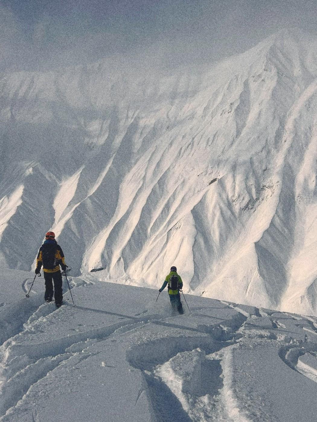 Two freeriders on a ridge above a large snowy face in the Gudauri backcountry.